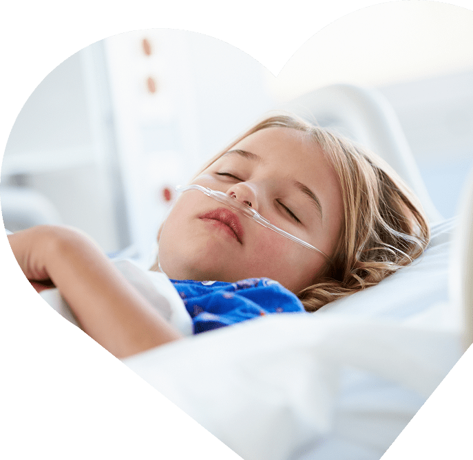 A young child with fair hair lies in a hospital bed at Sunflower Children’s Hospice, wearing a nasal oxygen tube and a blue gown, resting peacefully. The photo is framed in the shape of a heart.