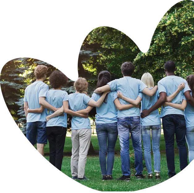 A group of eight people with arms around each other's backs stands on grass in a park, wearing matching light blue shirts and jeans. The scene, surrounded by trees, captures the supportive spirit of Sunflower Children’s Hospice.